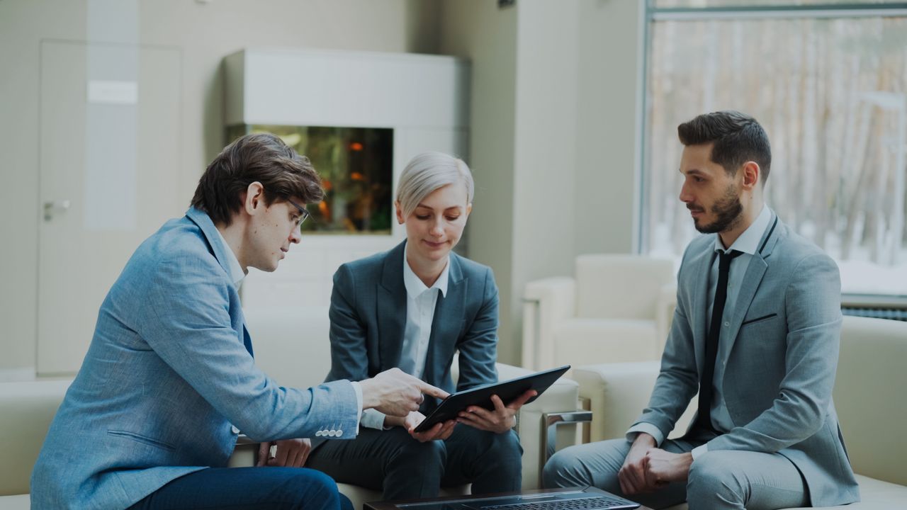 our-journey-02 Three professionals engaging in a business meeting in a modern office setting.