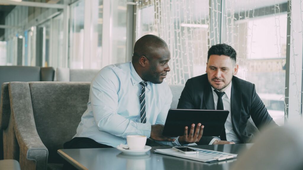 Two men in business attire collaborating over a tablet in a modern office setting.